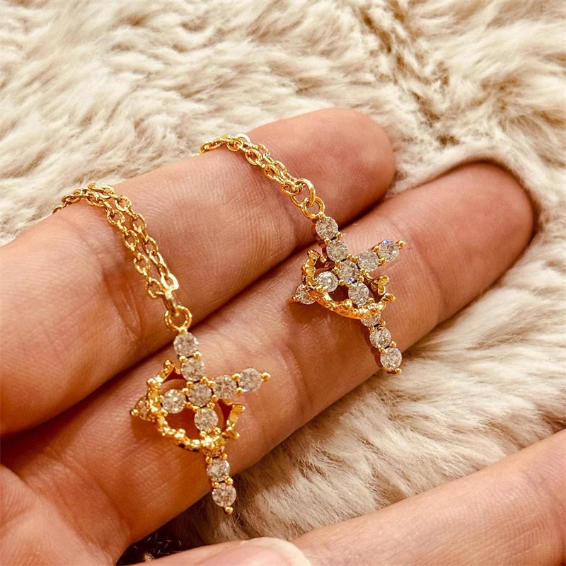 Two gold crown cross necklaces held in the hand
